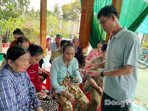 Đồng chí Nguyễn Thanh Bình hướng dẫn người dân ấp Hưng Hòa sử dụng điện thoại thông minh để đóng tiền bảo hiểm xã hội, bảo hiểm y tế và thanh toán không dùng tiền mặt.