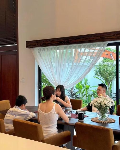 Không gian phòng ăn của gia đình nam ca sĩ được thiết kế theo phong cách hiện đại tối giản với tông màu trắng – nâu gỗ chủ đạo, tạo cảm giác ấm áp nhưng vẫn sang trọng. Bộ bàn ăn kích thước lớn đặt ngay cạnh hệ cửa kính kịch trần, mở ra khu vườn xanh mát bên ngoài. Ánh sáng tự nhiên tràn ngập căn phòng qua lớp rèm voan trắng mềm mại, khiến mọi góc nhỏ đều trở nên nhẹ nhàng và thư thái