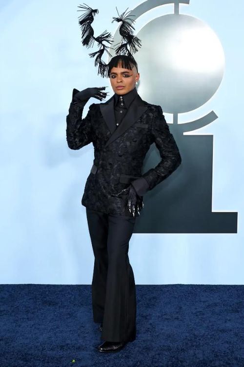 Layton Williams xuất hiện đầy phong cách với quần đen ống loe, áo khoác hai hàng khuy bằng vải gấm và phụ kiện đội đầu đính lông vũ nổi bật. Ảnh: Getty