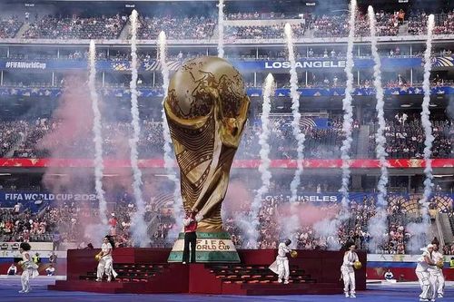 Mô hình Cup Vàng khổng lồ vươn lên giữa những cột pháo khói tại Los Angeles Stadium. Hình ảnh này thể hiện rõ ý tưởng “chiếc cúp phát sáng” dành riêng cho lễ khai mạc trên đất Mỹ.