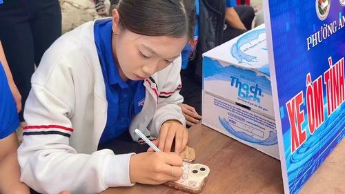Đoàn viên, thanh niên hỗ trợ thí sinh ghi thông tin cá nhân lên điện thoại trước khi gửi vào khu vực bảo quản. Ảnh: Minh Chí