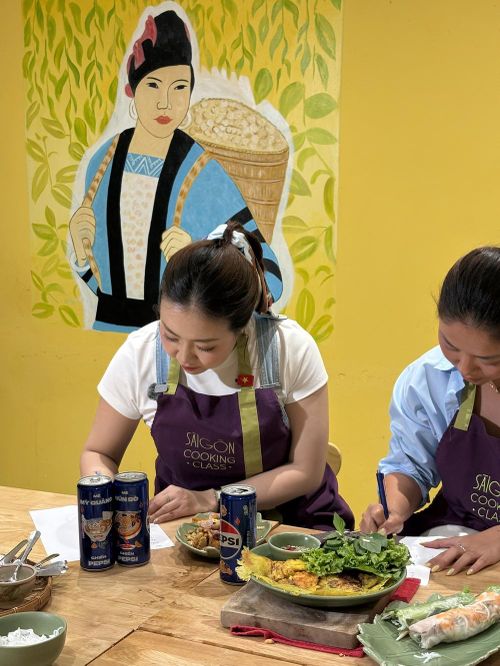 Phan Hoàng Kim - chủ kênh Ahihi Peekaboo và Nguyễn Ánh Xuân - chủ kênh Xuân Nghi đi chơi cùng chăm chú nghe chuyên gia ẩm thực chia sẻ, trước khi bắt tay vào thực hành làm các món bánh xèo, gỏi cuốn.