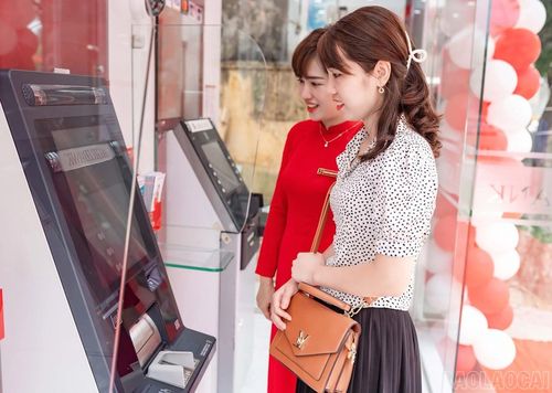 Nhân viên ngân hàng hướng dẫn khách hàng sử dụng máy gửi, rút tiền tự động.