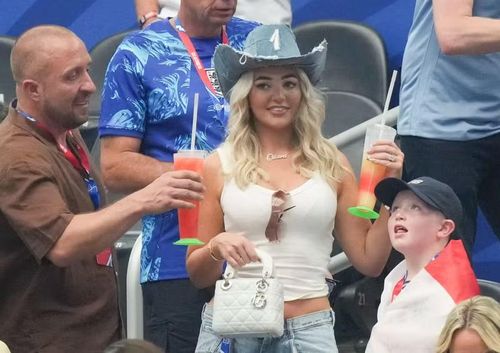 Ellie Watkins cầm những ly đồ uống lớn trên tay, hòa vào bầu không khí khá thoải mái của nhóm cổ động viên Anh. Đây là khoảnh khắc đời thường, đối lập với sức nóng của một trận đấu nhiều bàn thắng dưới sân.