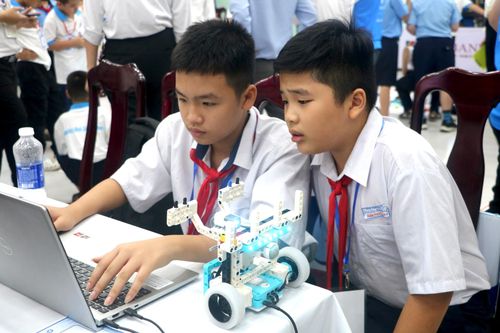 Các học sinh vừa lập trình trên phần mềm, vừa thử nghiệm trên sa bàn để robot vận hành hiệu quả. Ảnh: VĂN HOÀNG