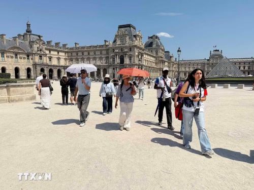 Nhiều du khách mang theo ô và nước uống khi tham quan bảo tàng Louvre trong đợt nắng nóng tại Paris. (Ảnh: Hữu Chiến/TTXVN)