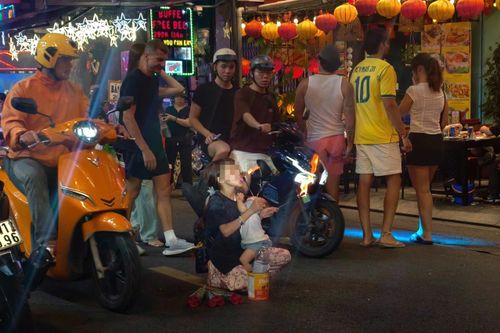  Một bé gái khoảng 12 tuổi bồng theo em nhỏ chừng 2 đến 3 tuổi, quỳ giữa lòng đường để biểu diễn thổi lửa. Trong khi quầng lửa bùng lên sát bên, em bé vẫn nằm gọn trong vòng tay người chị giữa dòng xe qua lại. Ảnh: NHÓM PV 
