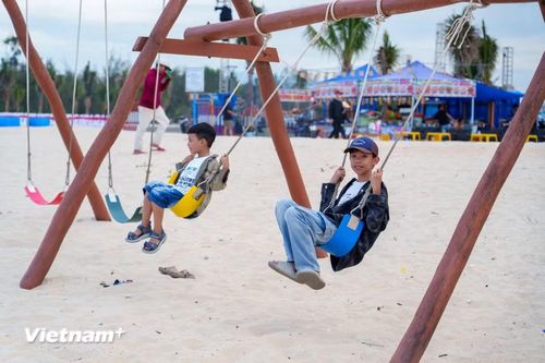 Các em nhỏ thích thú vui chơi trên những chiếc xích đu gỗ được bố trí ngay trên bãi cát trắng mịn của biển Hạ Thanh. (Ảnh: Thanh Phong/Vietnam+)