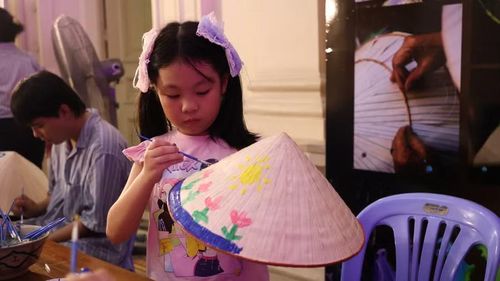 Em nhỏ chăm chú vẽ và trang trí nón lá truyền thống tại khu trải nghiệm nghề thủ. Ảnh: Khánh Trân.