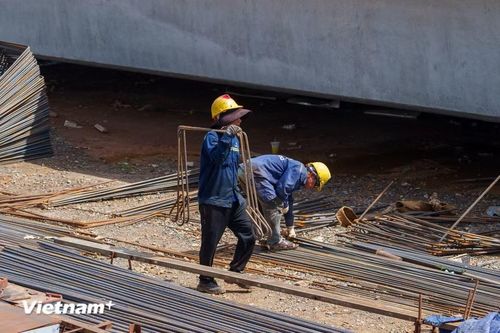 Thời tiết khắc nghiệt khiến công việc vác những bó thép nặng trĩu trên vai của người thợ càng trở nên vất vả, tốn rất nhiều sức lực. (Ảnh: Thanh Phong/Vietnam+)