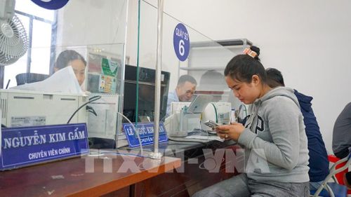 Người dân sử dụng điện thoại thông minh để thực hiện các thủ tục hành chính trực tuyến dưới sự hỗ trợ của cán bộ tại Trung tâm Phục vụ hành chính công phường Long Hoa, tỉnh Tây Ninh. Ảnh: Minh Phú – TTXVN