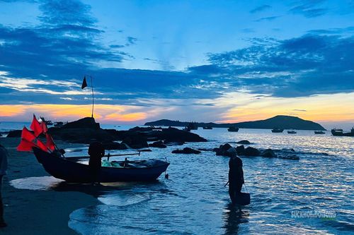 Một ngư dân xách túi hải sản từ mép nước lên bãi khi trời vừa sáng.