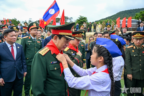Học sinh Trường Tiểu học Thongnamoun ở huyện Xaychamphone, tỉnh Bolykhamxay (Lào) đeo khăn quàng đỏ cho Đại tướng Phan Văn Giang và Đại tướng Khamliang Outhakaysone. 