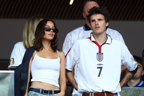 Cruz Beckham xuất hiện với áo đấu trắng cổ điển của tuyển Anh, phối cùng quần jeans xanh và thắt lưng da nâu, tạo phong cách casual vintage. Jackie Aposteln - bạn gái Cruz - diện áo tank-top trắng ôm sát kết hợp quần denim cạp thấp, kính râm mắt mèo và phụ kiện tối giản, mang đậm tinh thần Y2K.