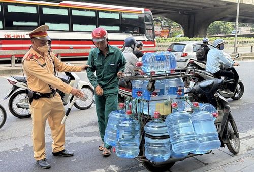 Một trường hợp xe máy chở nhiều bình nước làm che khuất biển số bị cán bộ Đội Cảnh sát giao thông số 7 yêu cầu dừng phương tiện và kiểm tra. Ảnh: Trung Nguyên - TTXVN