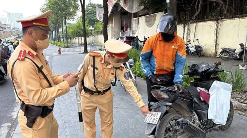 Cán bộ Đội Cảnh sát giao thông số 7 kiểm tra trường hợp biển số xe máy bị che, dán làm thay đổi chữ và số. Ảnh: Trung Nguyên - TTXVN