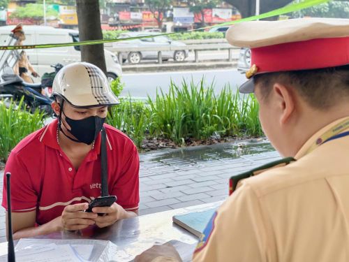 Cán bộ Đội Cảnh sát giao thông số 7 (Phòng Cảnh sát giao thông Công an thành phố Hà Nội) lập biên bản một tài xế giao hàng vi phạm quy định về biển số xe. Ảnh: Trung Nguyên - TTXVN