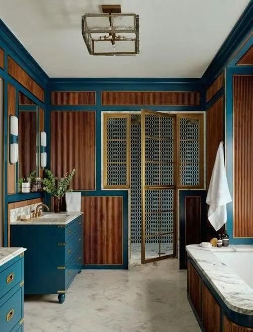 Phòng tắm được cải tạo hoàn toàn với bồn tắm ngâm, khu tắm đứng riêng và hai bàn trang điểm đặt làm theo yêu cầu. Gỗ óc chó có vân sọc kết hợp cùng đá cẩm thạch và các chi tiết đồng đánh bóng mang lại cảm giác ấm áp, mềm mại cho không gian vốn sử dụng nhiều vật liệu cứng. Hai tủ lavabo màu xanh ngọc tạo điểm nhấn nhẹ nhàng nhưng đủ khác biệt trong tổng thể.