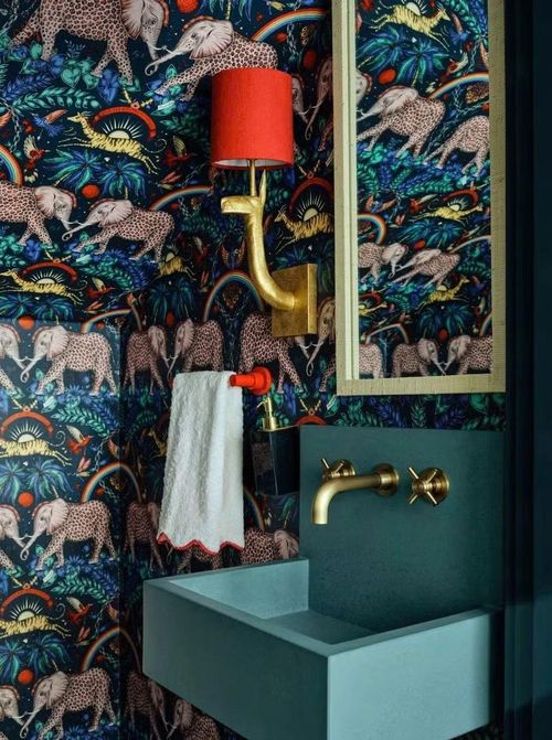 Giấy dán tường Kravet với họa tiết phong phú bao phủ không gian nhỏ gọn, trong khi bồn rửa bằng bê tông treo tường của Concretti tạo nên một yếu tố điêu khắc bất ngờ trên nền tường đầy màu sắc.
