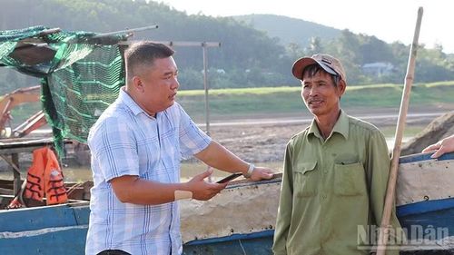 Phóng viên Báo Nhân Dân (bên trái) trao đổi thông tin với ông Nguyễn Đình Long - người lái chiếc thuyền nan đưa đón người dân qua lại sông ở bến Đá Giăng ngay từ những ngày đầu.