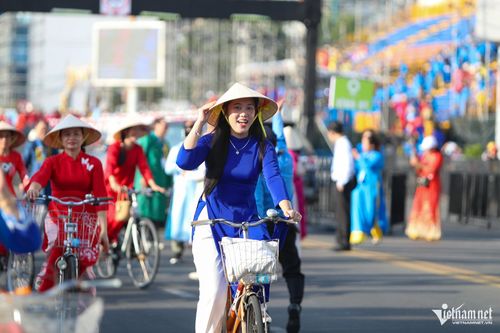 Cô gái nở nụ cười rạng rỡ trong trang phục áo dài, đạp xe diễu hành. Ảnh: Xuân Ngọc