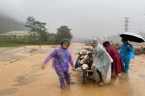 Nhiều người dân đội mưa khiêng chiếc xe máy đã bị bùn lầy, đất và rác vùi lấp, di chuyển về nơi an toàn.