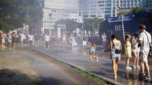 Người dân làm mát cơ thể dưới làn nước phun từ vòi rồng của cảnh sát tại quảng trường Potsdamer Platz, Berlin (Đức), ngày 27-6-2026. Ảnh: news.cgtn.com