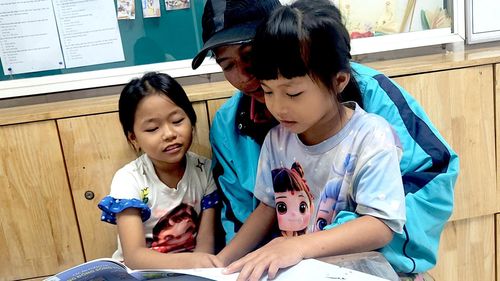 Yến Nhi (bên trái) đọc truyện cùng cha và em gái trong khi chờ đến ca chạy thận.