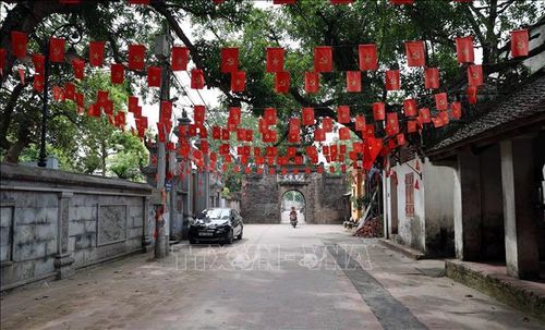 Không gian bên trong làng Ước Lễ với tuyến đường gạch cổ dẫn ra cổng làng, rợp cờ Tổ quốc và cờ Đảng, lưu giữ đậm nét kiến trúc truyền thống của một làng cổ vùng đồng bằng Bắc Bộ.