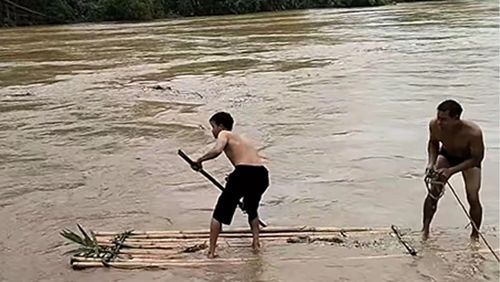 Hai người đàn ông đi mảng trên dòng suối cuộn chảy sau lũ để vớt gia súc. (Ảnh: Mạng xã hội)