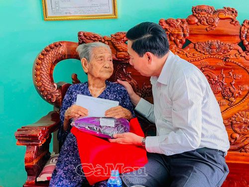 Đồng chí Nguyễn Quốc Tiến, Bí thư Đảng ủy, Chủ tịch HĐND xã Khánh Bình, trao quà tri ân gồm bộ áo dài và các sản phẩm dinh dưỡng tặng Mẹ Việt Nam anh hùng Nguyễn Thị Chữ (Ấp 6).