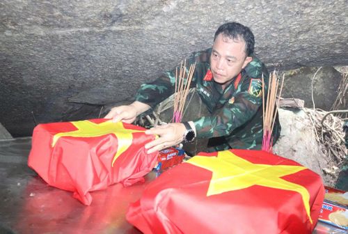 Đại tá Trần Hữu Ích, Chỉ huy trưởng Bộ CHQS TP Đà Nẵng thực hiện nghi thức phủ Quốc kỳ lên hài cốt liệt sĩ vừa được quy tập trong hang Đá Sập.