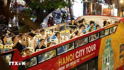 Đông đảo du khách trong và ngoài nước thích thú ngắm nhìn toàn cảnh không gian Hà Nội về đêm từ không gian mở trên tầng 2 của xe bus du lịch (Hanoi City Tour). Việc đưa vào vận hành và đẩy mạnh các tour ngắm cảnh đêm (Night Tour) bằng phương tiện hiện đại không chỉ làm đa dạng hóa các lựa chọn trải nghiệm cho du khách khi thành phố lên đèn, mà còn đóng vai trò như một "mạch máu" giao thông kết nối hiệu quả các điểm đến di sản văn hóa, ẩm thực và thương mại sầm uất trong chuỗi hệ sinh thái kinh tế đêm của Thủ đô. (Ảnh: Tiến Long/TTXVN phát)