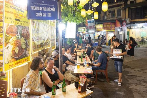 Du khách quốc tế thưởng thức ẩm thực đường phố tại khu vực được gắn biển "Tuyến phố an toàn thực phẩm có kiểm soát". Việc chuẩn hóa các quy trình vệ sinh an toàn thực phẩm và công khai thông tin quản lý tại các tuyến phố kinh doanh ăn uống về đêm giúp nâng cao chất lượng dịch vụ, tạo sự yên tâm cho du khách khi trải nghiệm ẩm thực Thủ đô. (Ảnh: Tiến Long/TTXVN phát)