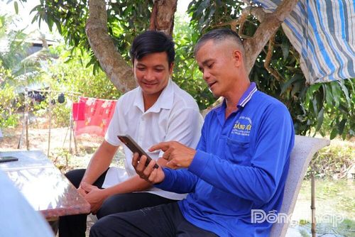 Anh Nguyễn Anh Tuấn (bên phải), nông dân ấp Mỹ Long 4, xã Mỹ Hiệp theo dõi dữ liệu từ hệ thống quan trắc thông minh trên điện thoại để chủ động chăm sóc vườn cây.