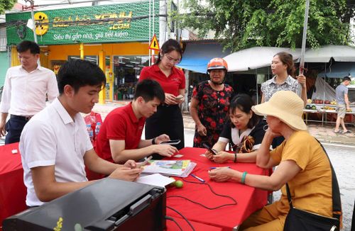 Cán bộ Agribank Chi nhánh Mỹ Đức hỗ trợ người dân xã Phúc Sơn làm thủ tục mở tài khoản, cài đặt ứng dụng thanh toán không dùng tiền mặt. Ảnh: Kim Nhuệ
