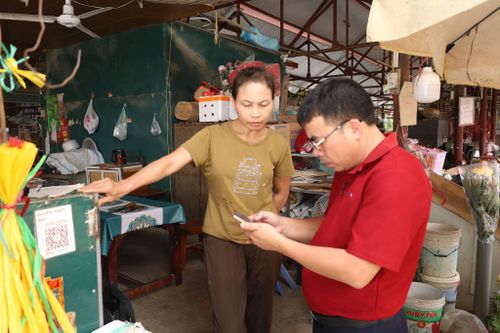 Cán bộ Agribank hỗ trợ tiểu thương ở chợ Thượng Lâm (xã Phúc Sơn) cài đặt ứng dụng Agribank Plus. Ảnh: Kim Nhuệ