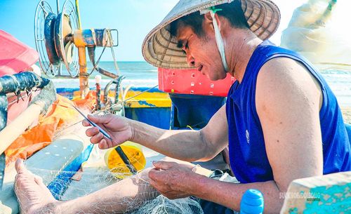 Công việc vá lưới được thực hiện ngay trên thuyền thúng. Ảnh: Lâm Nguyễn