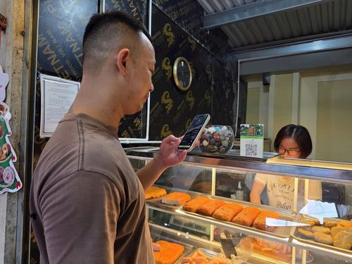 Khách mua giò chả quét mã thanh toán ở quầy hàng của chị Nguyễn Thị Lan tại chợ Trung tâm xã Đông Anh. Ảnh: Mai Khôi.