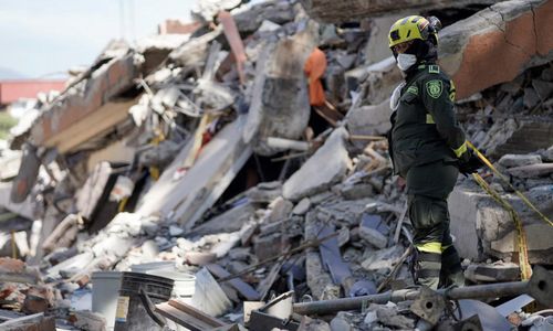 Nhân viên cứu hộ trước những đống đổ nát của các toà nhà - Ảnh: Reuters