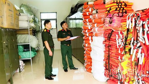 Thiếu tá Phan Ngọc Sang (bên phải) kiểm tra vật tư, trang thiết bị phòng, chống thiên tai tại kho tập kết của Ban CHQS xã Vĩnh Thành.