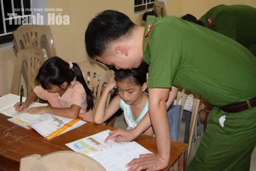Cán bộ Công an xã Lương Sơn hướng dẫn học sinh làm bài tại “Lớp học 0 đồng” ở nhà văn hóa thôn Ngọc Quang.