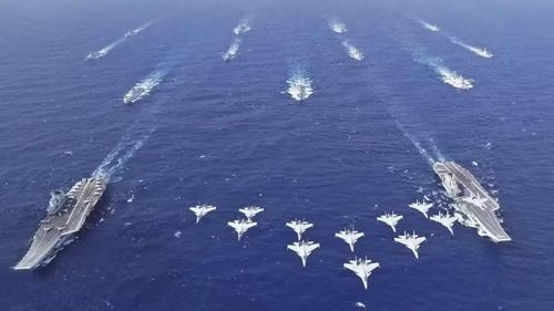 Tàu Liêu Ninh (trái) và tàu Sơn Đông (phải) với các tiêm kích hạm J-15 bay phía trên. Ảnh: TWZ.