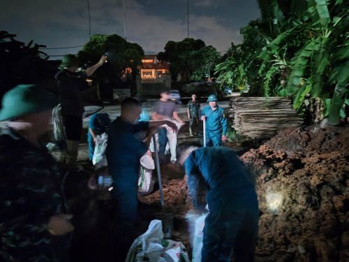 Lực lượng chức năng xã Hạ Bằng đắp đất và các bao cát ngăn nước lũ tràn vào khu dân cư đêm 24-8. Ảnh: HOA PHƯƠNG