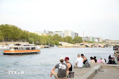 Người dân ngồi thư giãn sát mép nước, ngắm nhìn tàu thuyền chở du khách qua lại trên sông Seine. (Ảnh: Hữu Chiến /TTXVN)