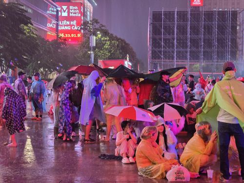Nhiều cổ động viên dùng áo mưa, ô và bạt che tạm khi trời bất ngờ đổ mưa