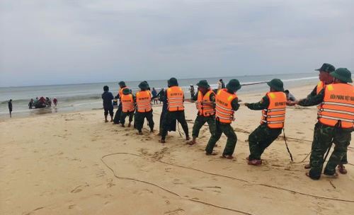 Đồn Biên phòng Cửa khẩu cảng Cửa Việt hỗ trợ ngư dân kéo thuyền đánh cá bị sóng đánh chìm trên biển vào bờ. (Ảnh: H.M)
