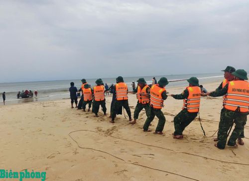 Cán bộ, chiến sĩ Đồn Biên phòng cửa khẩu cảng Cửa Việt hỗ trợ ngư dân xã Cửa Việt kéo thuyền bị chìm vào bờ. Ảnh: Hoài Nam