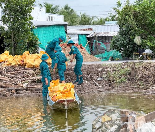 Dân quân Ban CHQS xã Khánh Bình hỗ trợ vận chuyển vật tư bằng xuồng qua sông giúp nhà dân trong quá trình xây dựng.