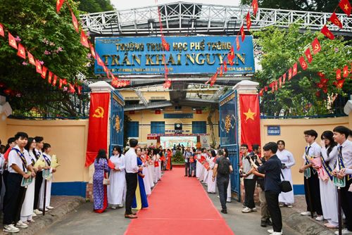 Dù là cuối tuần, khi đồng hồ chưa điểm 6h, cổng trường THPT Trần Khai Nguyên đã rộn ràng, ngập tràn tiếng nói cười. Cờ hoa được trang trí dọc lối vào, từng tốp học sinh trong đồng phục lần lượt di chuyển, nhanh chóng tìm về vị trí của lớp. Trong sân, giáo viên và nhân viên nhà trường tất bật kiểm tra sân khấu, màn hình và hệ thống âm thanh để chuẩn bị cho chương trình khai giảng. Tiếng loa phát thử vang lên giữa sân trường, xen lẫn với tiếng trò chuyện, gọi nhau của học sinh, báo hiệu lễ khai giảng năm học mới chính thức bắt đầu.